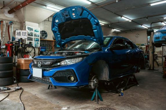 A blue Honda Civic with its hood open on a lift in a garage