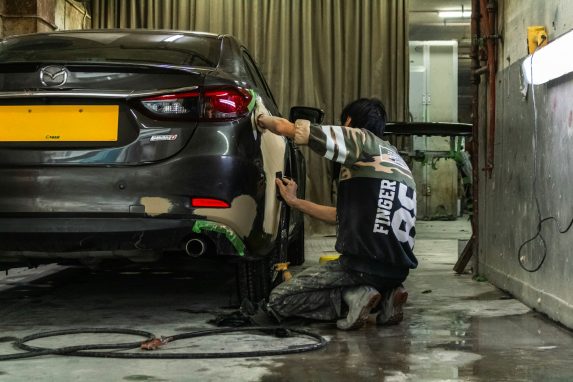 A person sanding the rear panel of a grey car in a workshop