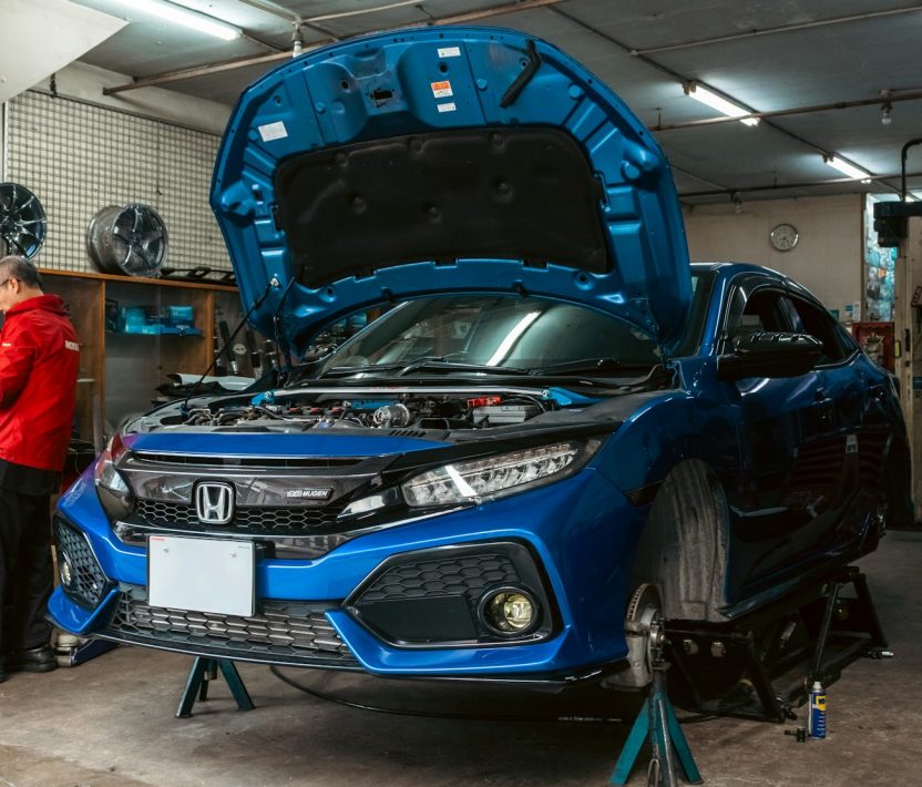 A mechanic in a red jacket working on a blue car in a garage