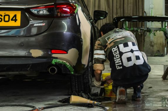 A person in a camouflage shirt repairing a car bumper in a workshop
