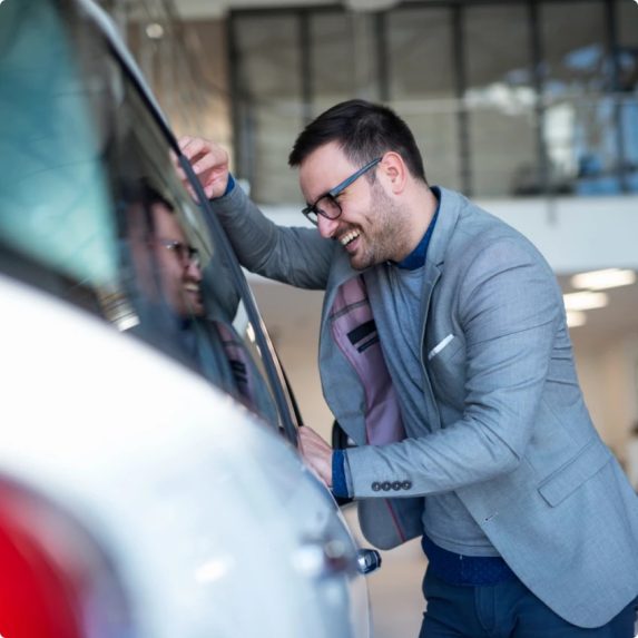 Uśmiechnięty mężczyzna oglądający białe auto w salonie samochodowym
